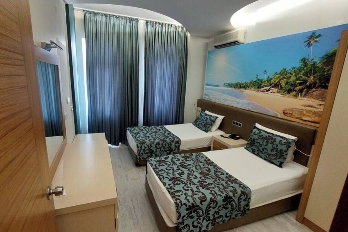 A hotel room with two beds, a desk, and a large beach mural on the wall.