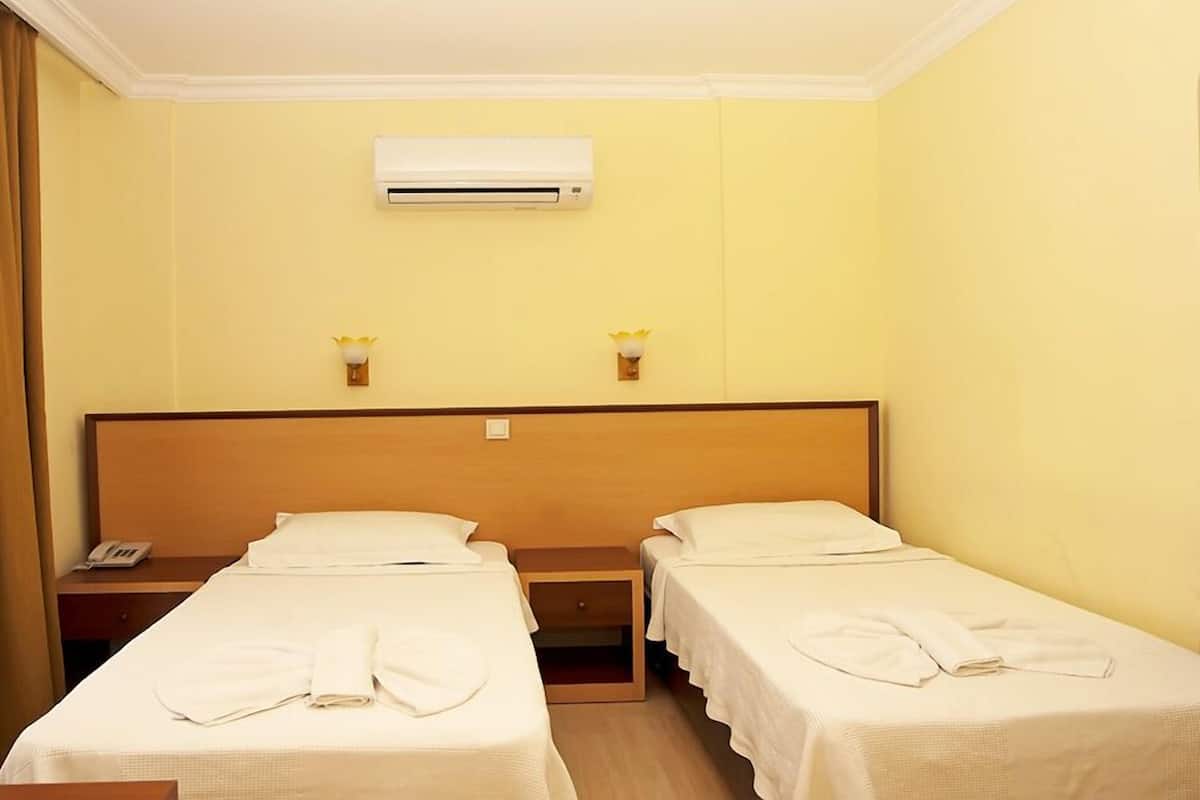 A hotel room with two single beds, a wooden headboard, an air conditioning unit, and bedside lamps.