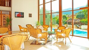 A spacious room with wicker furniture, large windows, and a view of a swimming pool.