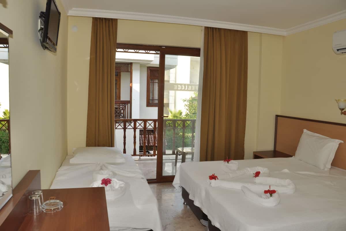 A hotel room with two beds, a wooden nightstand, a desk with a chair, and a balcony with a view.