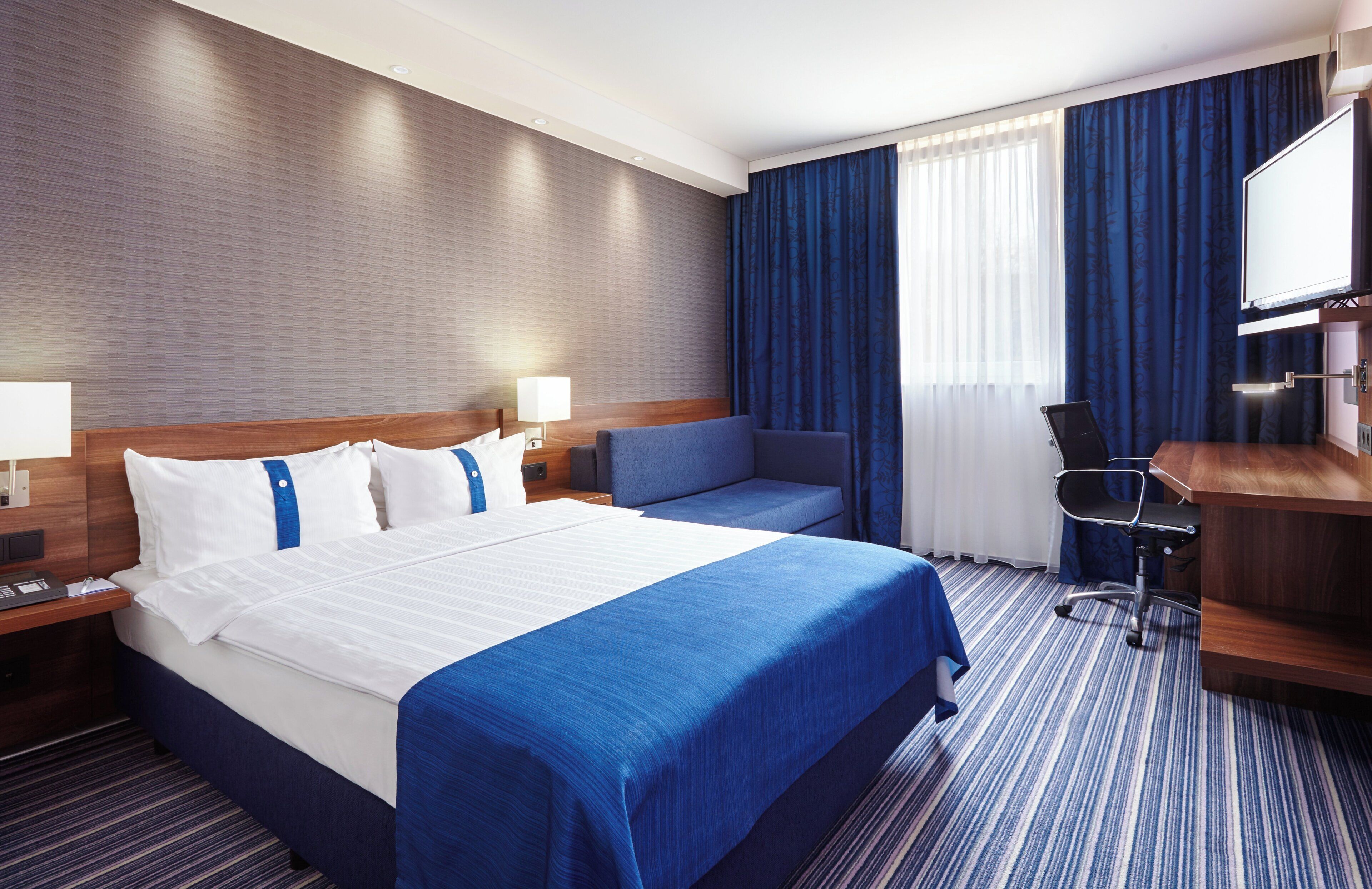 Une chambre d’hôtel avec un grand lit, un bureau, une chaise et un téléviseur.