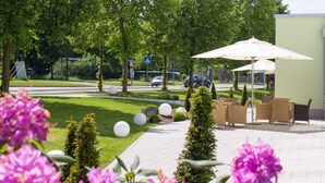 Un espacio al aire libre con pavimento, mobiliario y sombrillas, rodeado de follaje y flores.