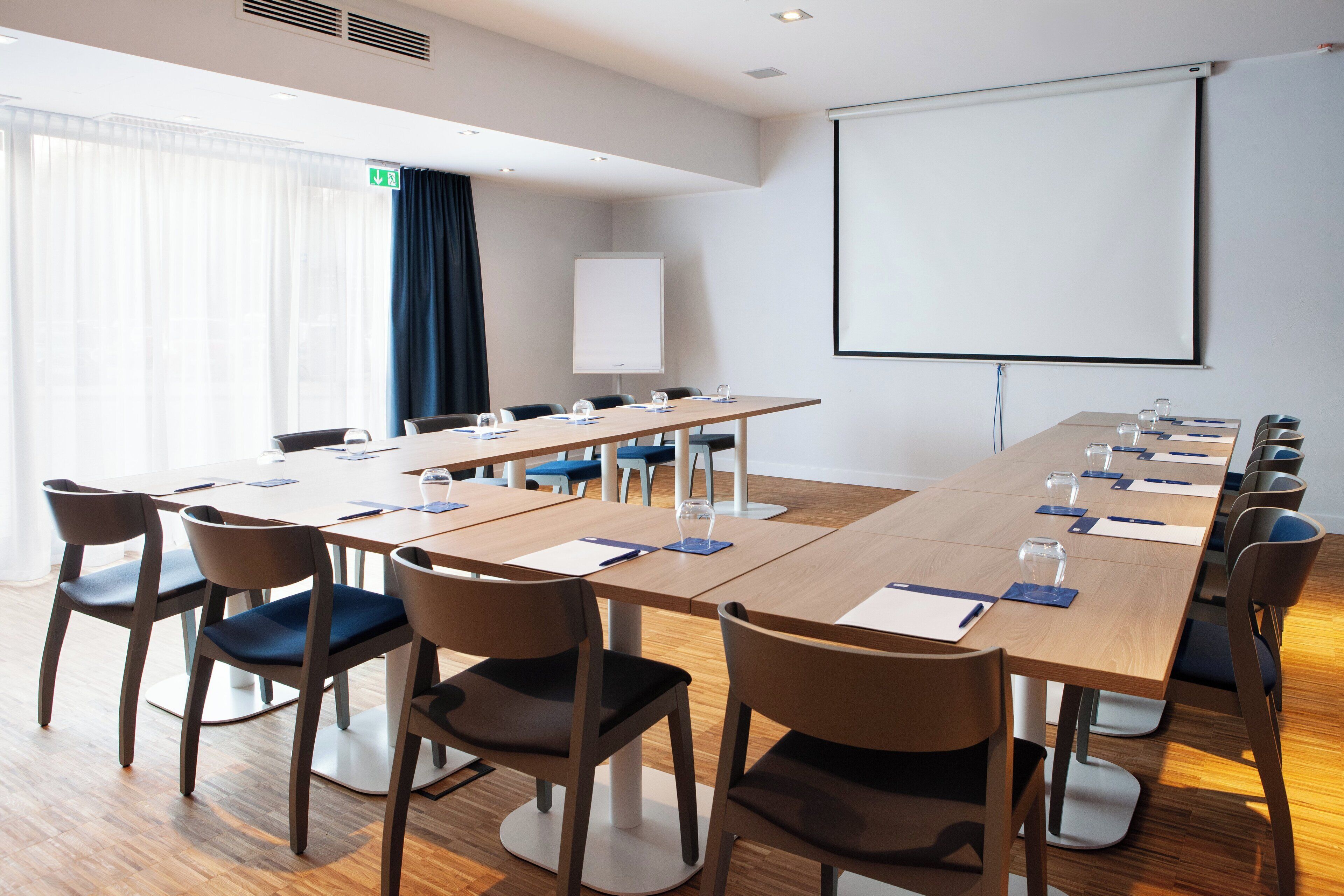 Une salle de conférence équipée d’une longue table, de chaises, d’un écran de projection et d’un tableau blanc.