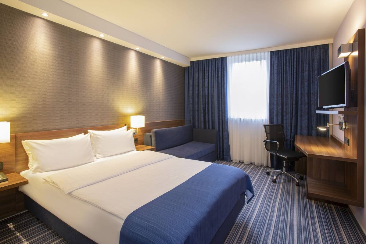A hotel room with a large bed, a desk, a chair, and a television.