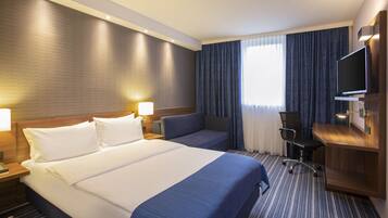 A hotel room with a large bed, a desk, a chair, and a television.