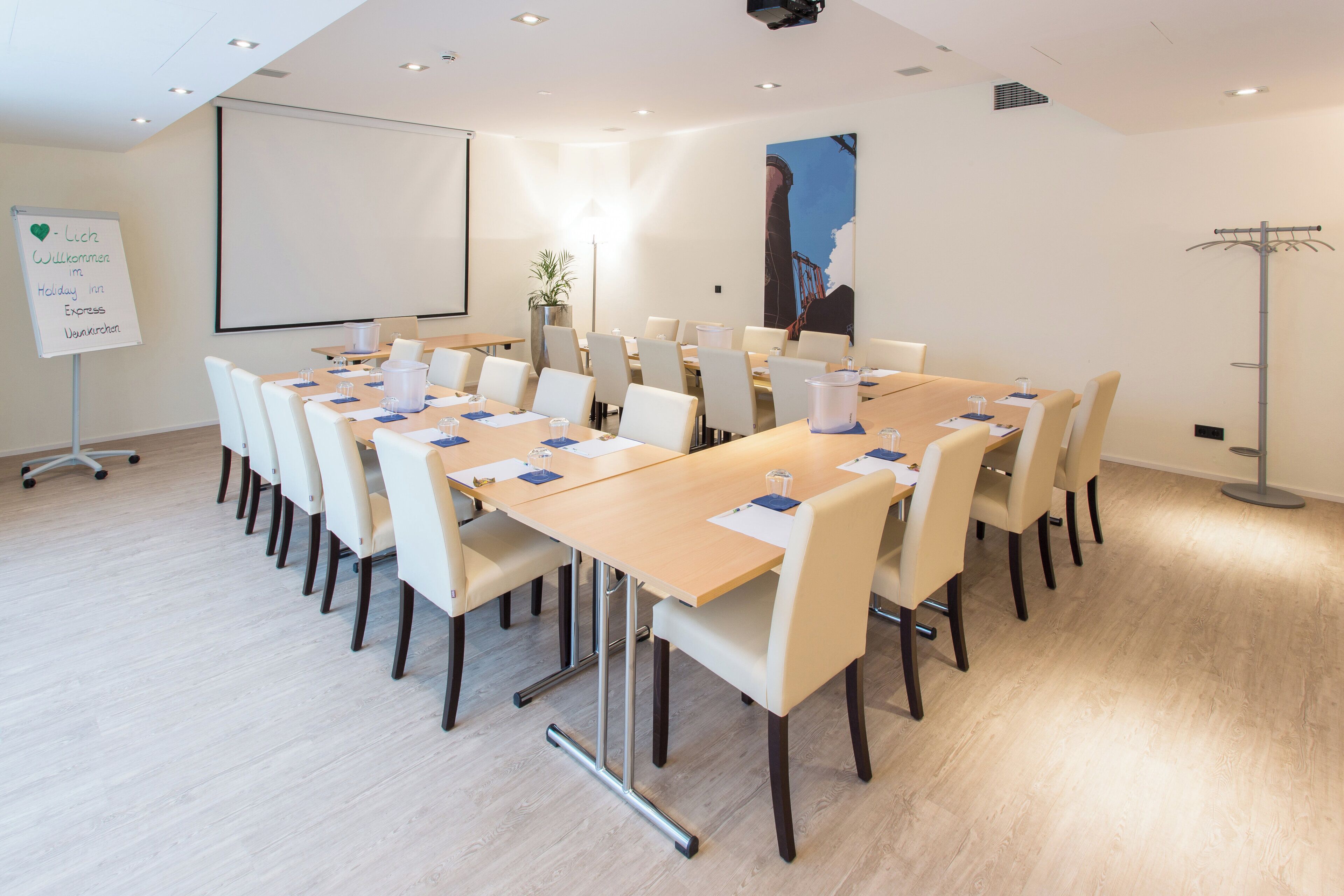 Ein Konferenzraum mit einem langen Tisch, Stühlen, einer Tafel und einer Projektionsleinwand.