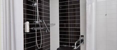 Ein modernes Badezimmer mit schwarzen Fliesenwänden, einer Dusche mit Duschbrause, einem schwarzen Handtuchhalter und einem weiß gefliesten Boden.