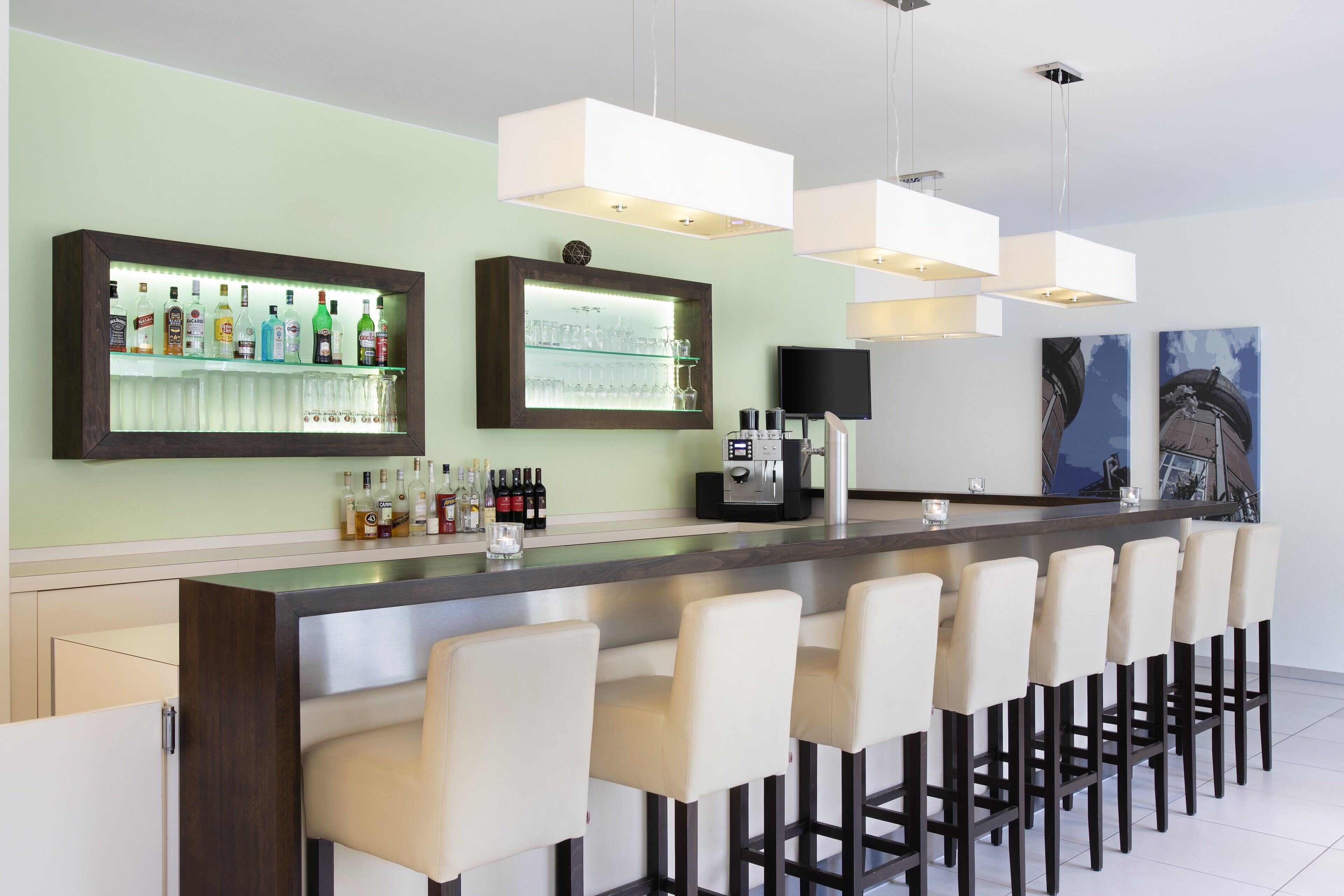 Un área de bar moderna con una barra larga, diversas opciones de asientos y una variedad de botellas de licor.