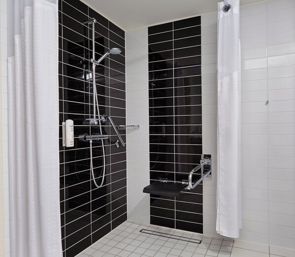 A modern bathroom with black tiled walls, a shower with a handheld showerhead, and a toilet with a chrome faucet.