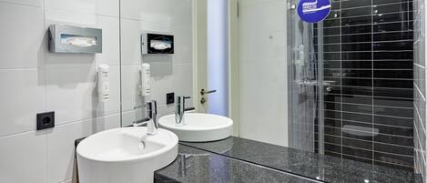 A modern bathroom with two sinks, a mirror, and a glass-enclosed shower.