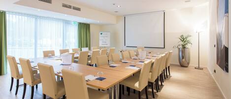A conference room with a long table, chairs, a whiteboard, and a projector screen.