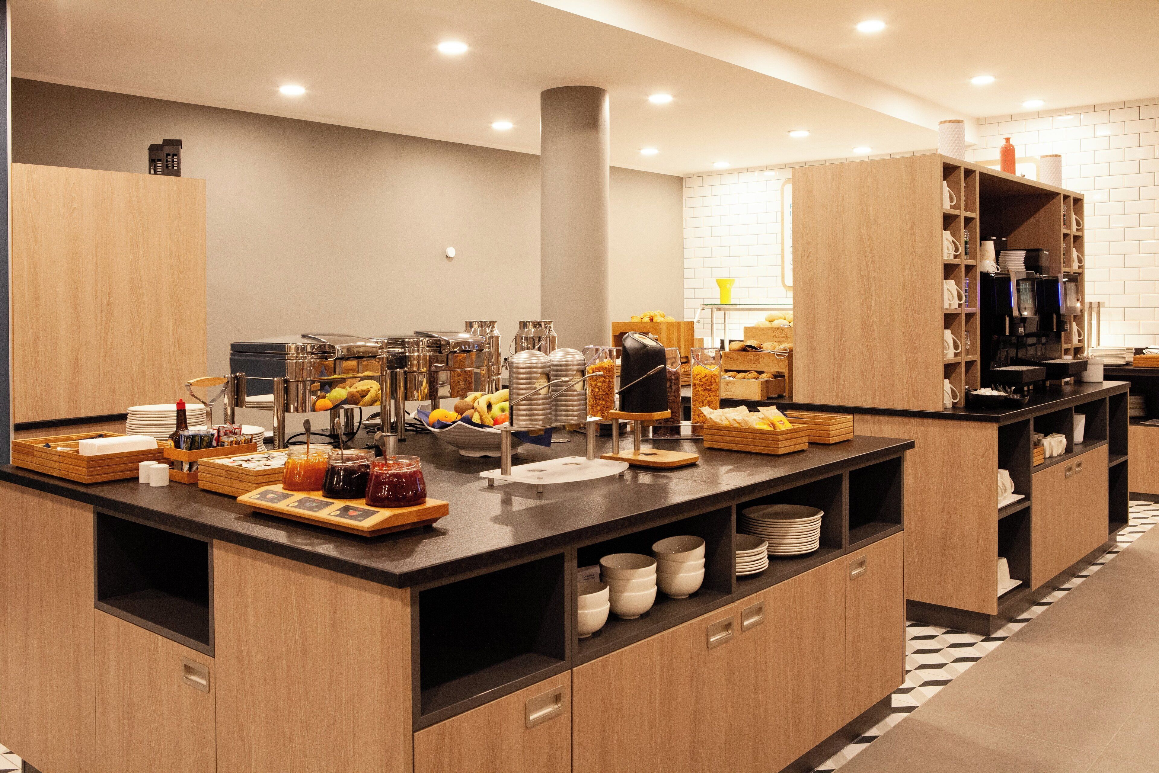 A modern breakfast bar with a variety of food items and beverages, wooden cabinets, and a clean, tiled floor.