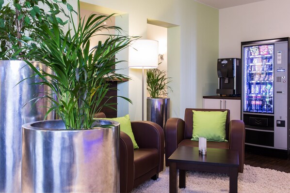 A modern living room with a sofa, armchairs, a coffee machine, and a plant in a metallic planter.
