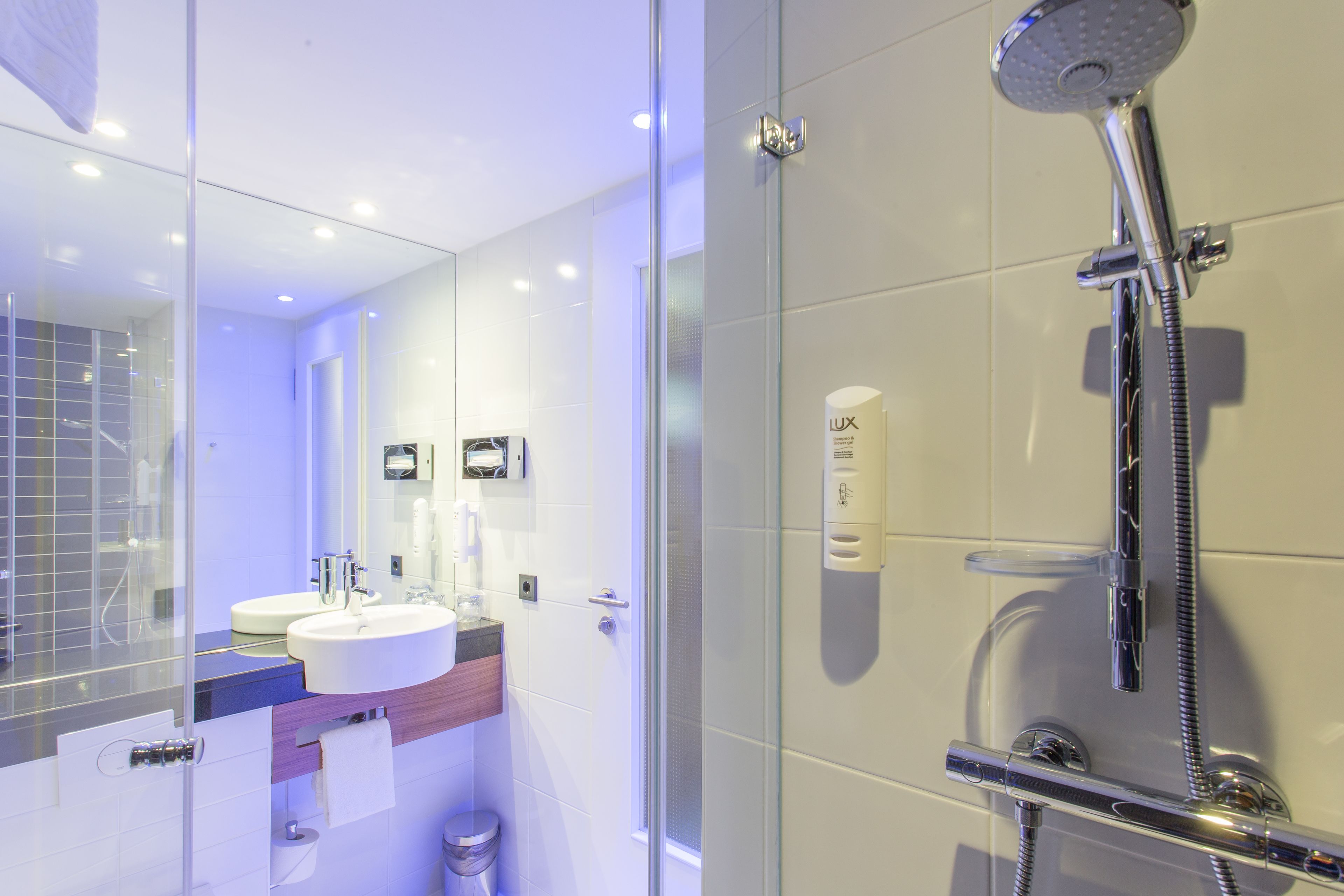 Een moderne badkamer met een douchecabine van glas, een wastafel met spiegel en een handdoekdispenser.