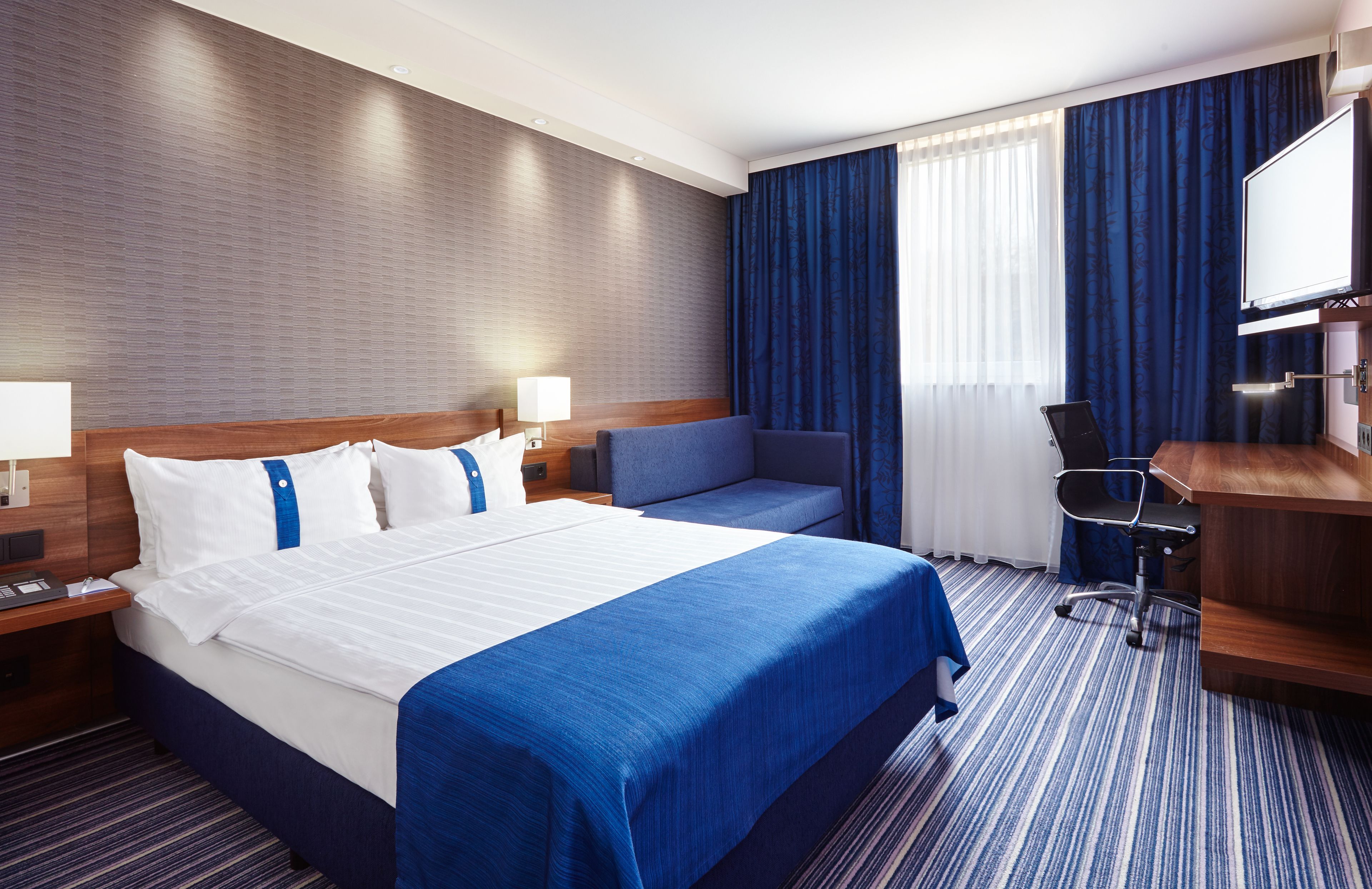 Una habitación de hotel con una cama grande, un escritorio, una silla y un televisor.