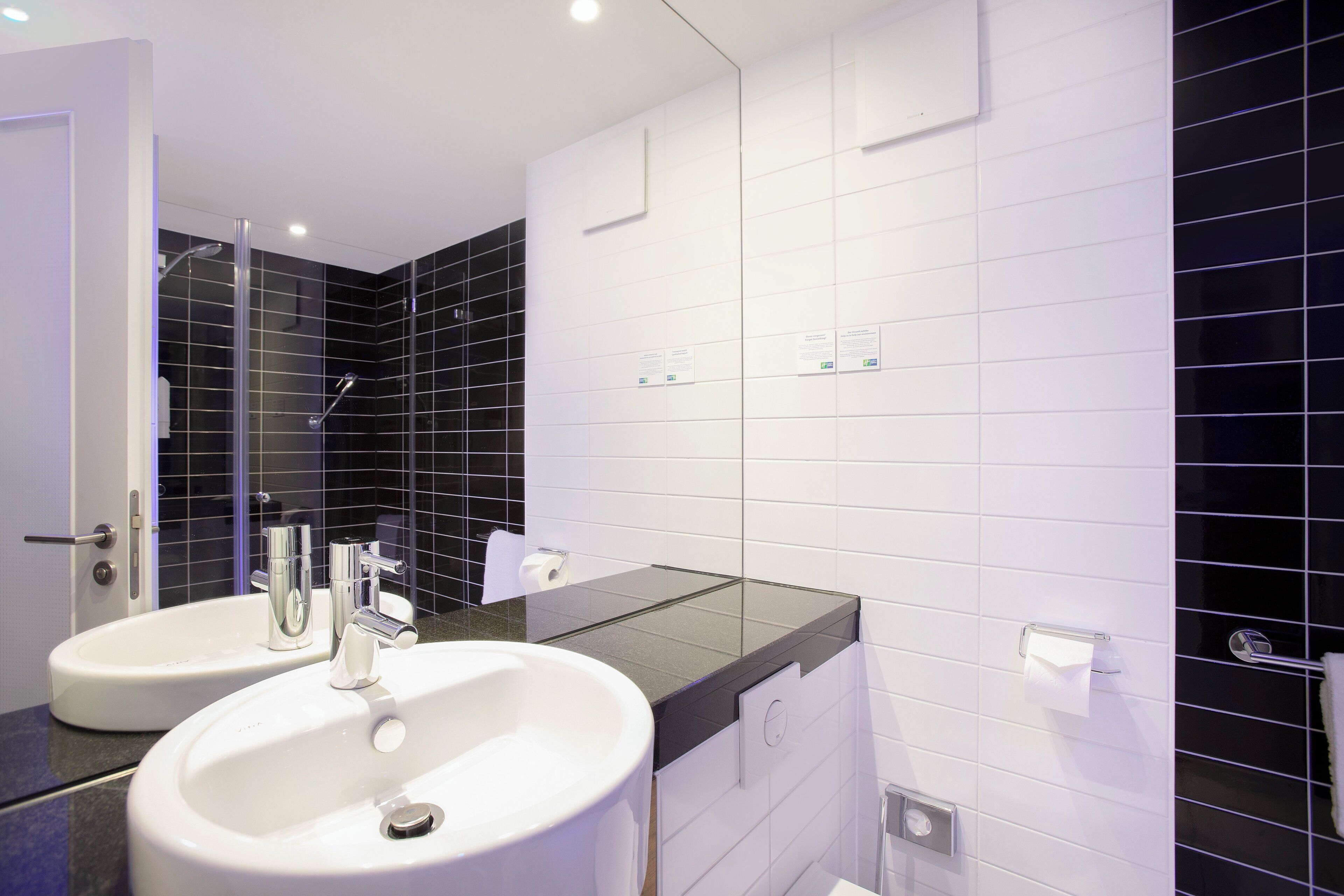 A modern bathroom with two sinks, a glass shower enclosure, and white tiled walls.
