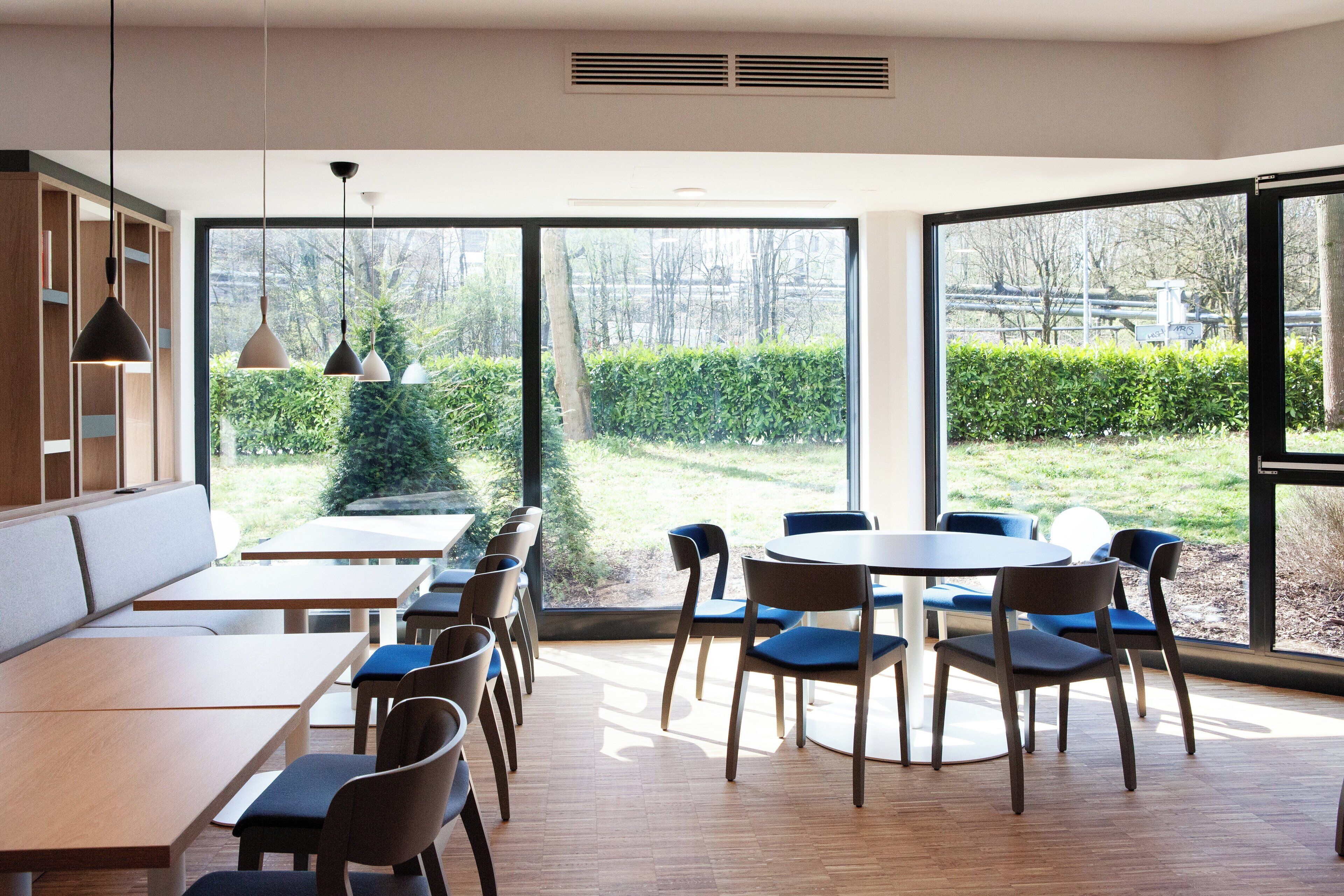 A modern dining area with large windows, wooden tables, and chairs.