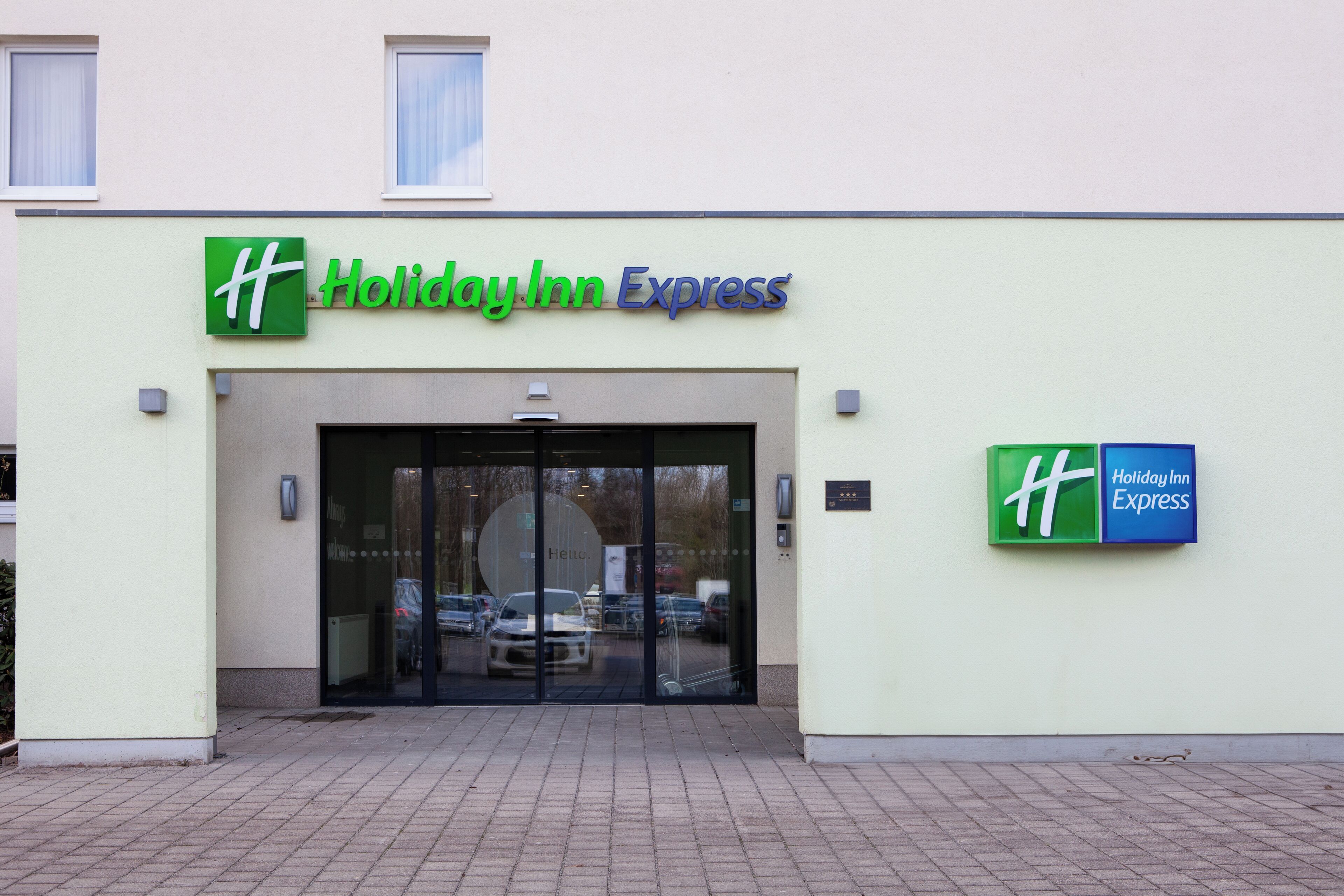 Het uiterlijk van een Holiday Inn Express hotel met een groen- en blauw logo, een glazen ingang en een verharde oprit.