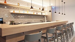 Un área de bar moderna con una barra alargada, varios taburetes y lámparas colgantes.