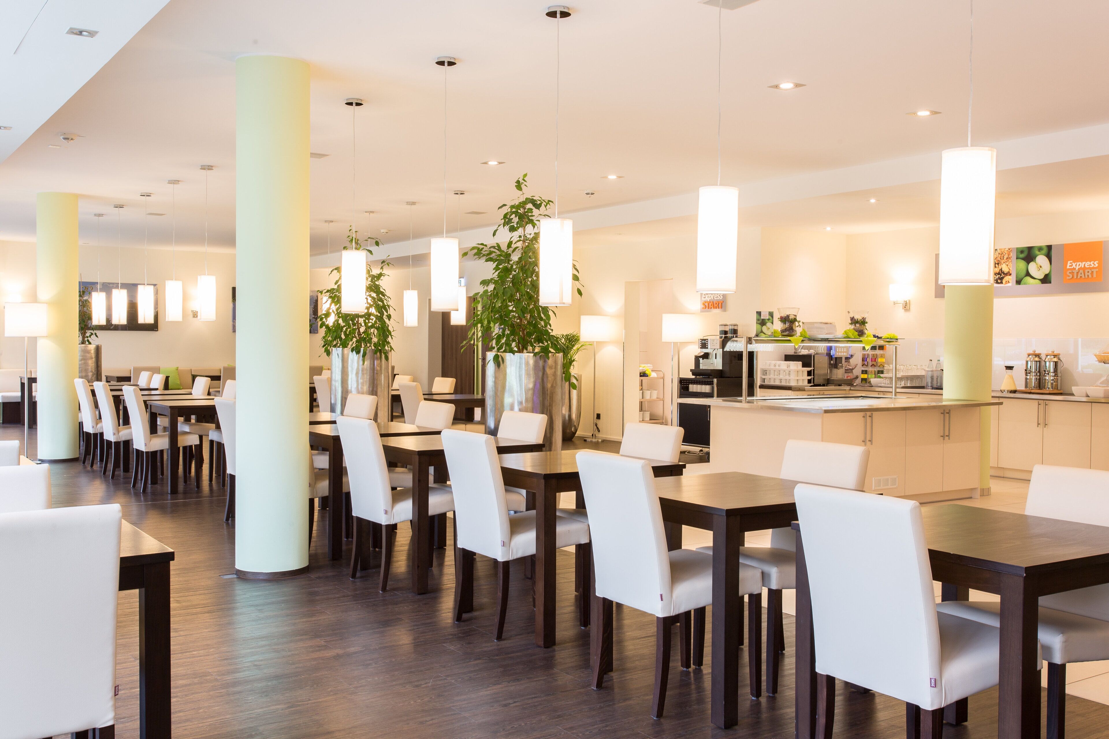 A modern dining area with tables and chairs, pendant lighting, and a kitchen in the background.