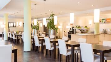A modern dining area with tables and chairs, pendant lighting, and a kitchen in the background.