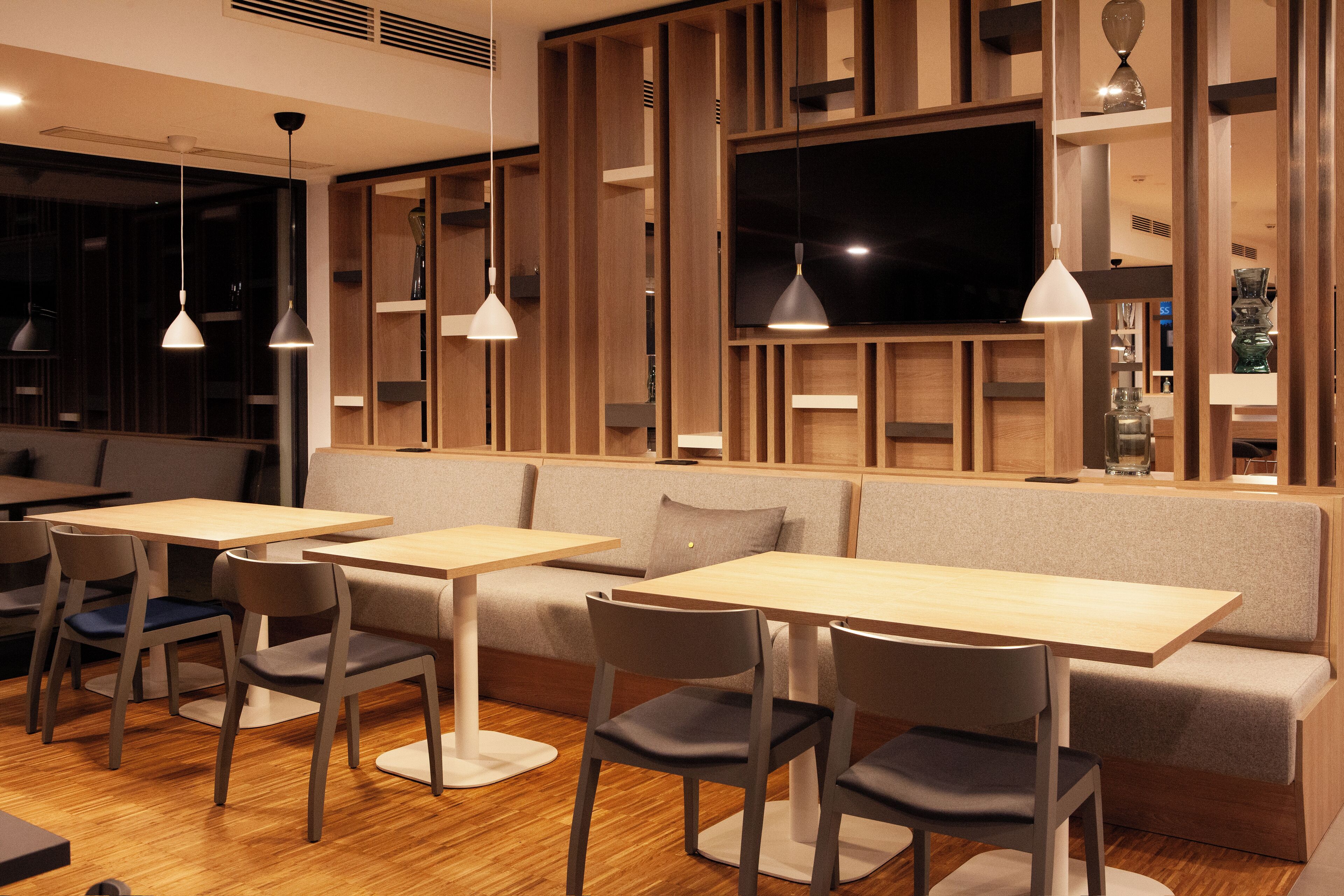 Un restaurante moderno con paneles de madera, una pantalla de televisión grande y una zona de estar con mesas y sillas.