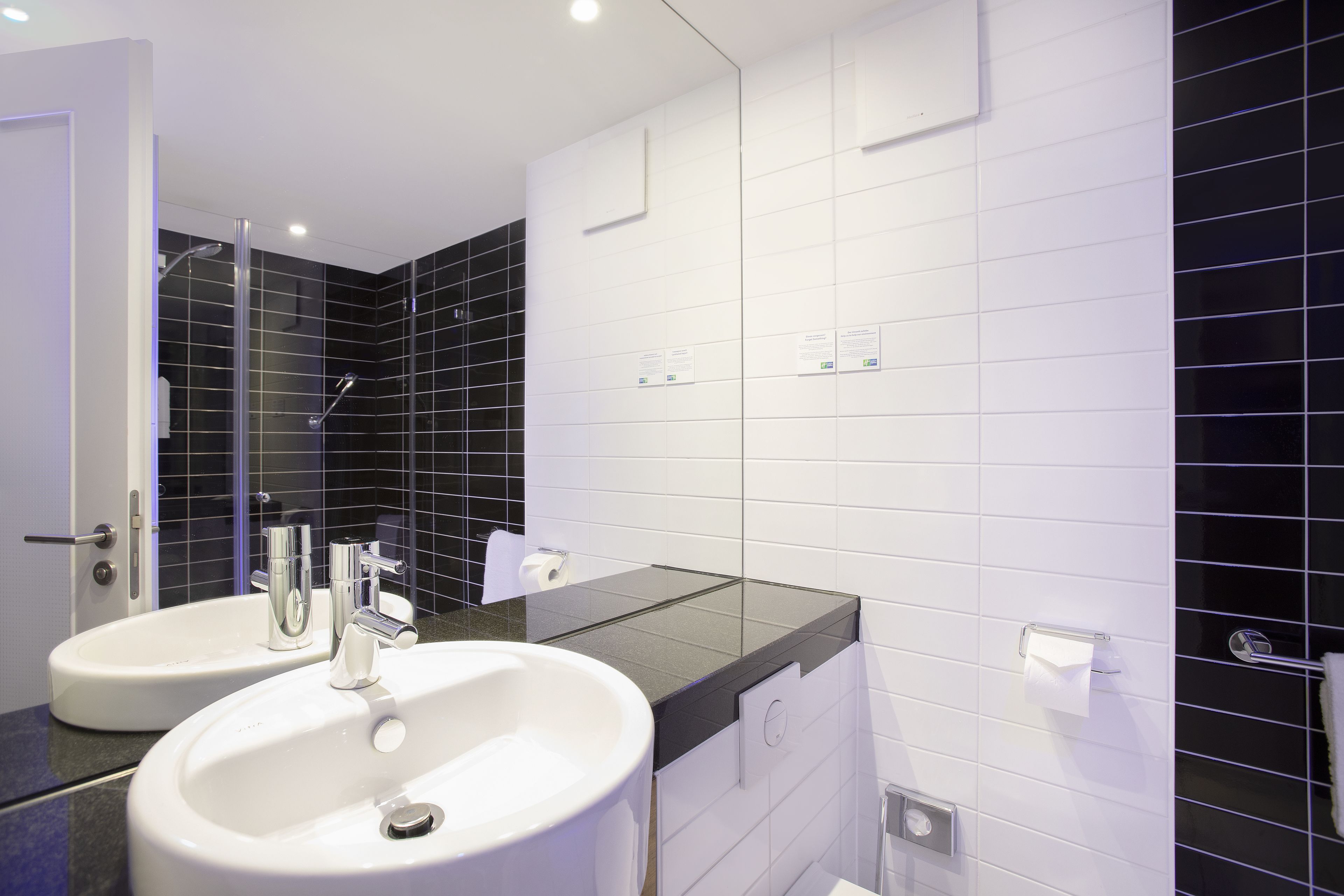 Un baño moderno con dos lavamanos, cabina de ducha de vidrio y paredes de azulejos blancos.