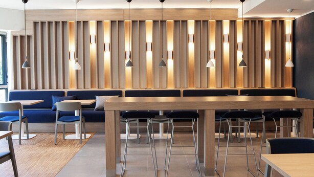Un restaurante moderno con una larga mesa de madera, asientos azules e iluminación colgante.