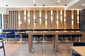 A modern restaurant with a long wooden table, blue seating, and pendant lighting.