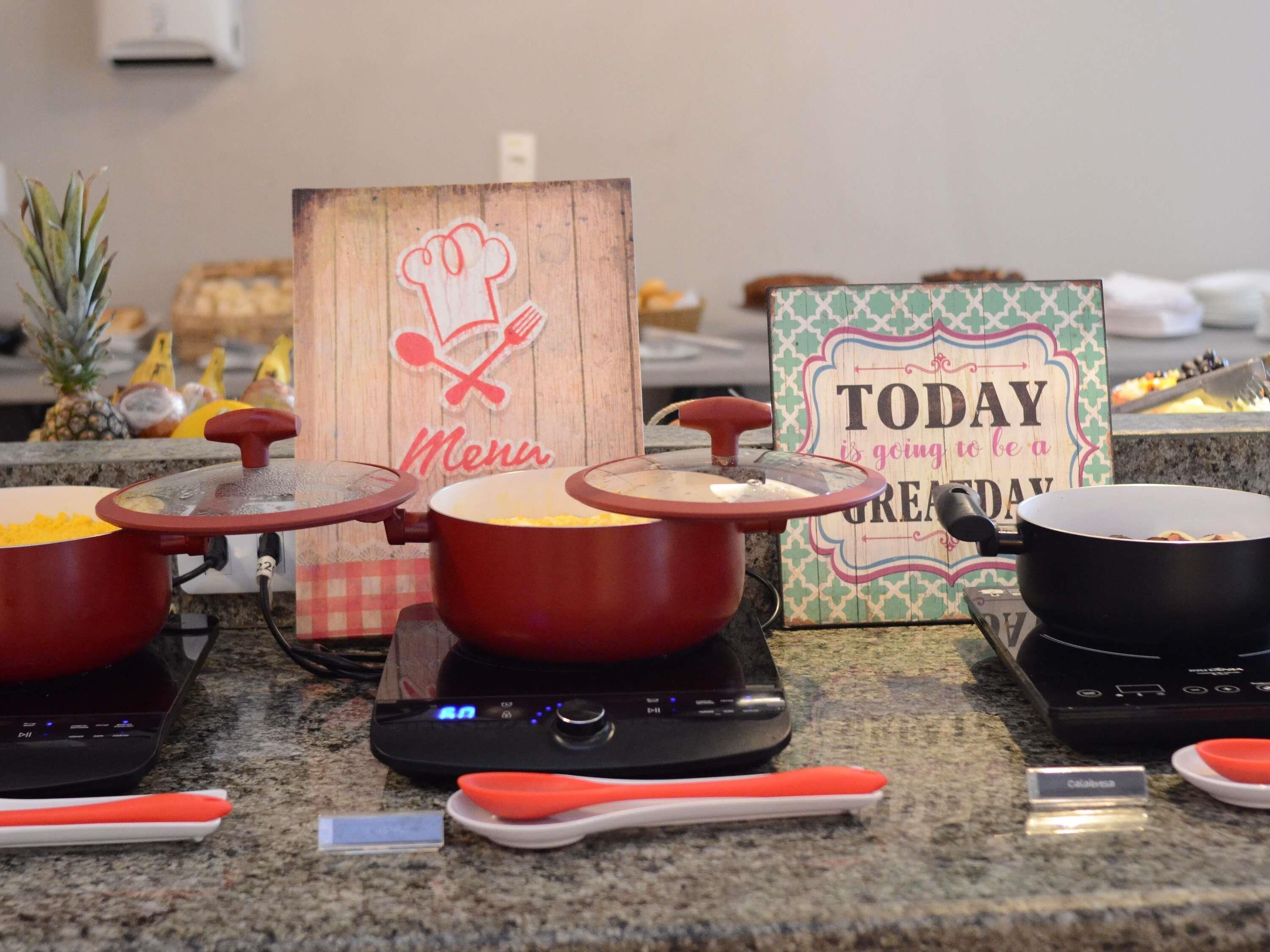 Una cocina con varias placas de inducción, utensilios de cocina y un letrero de madera con un sombrero de chef y cubiertos cruzados.