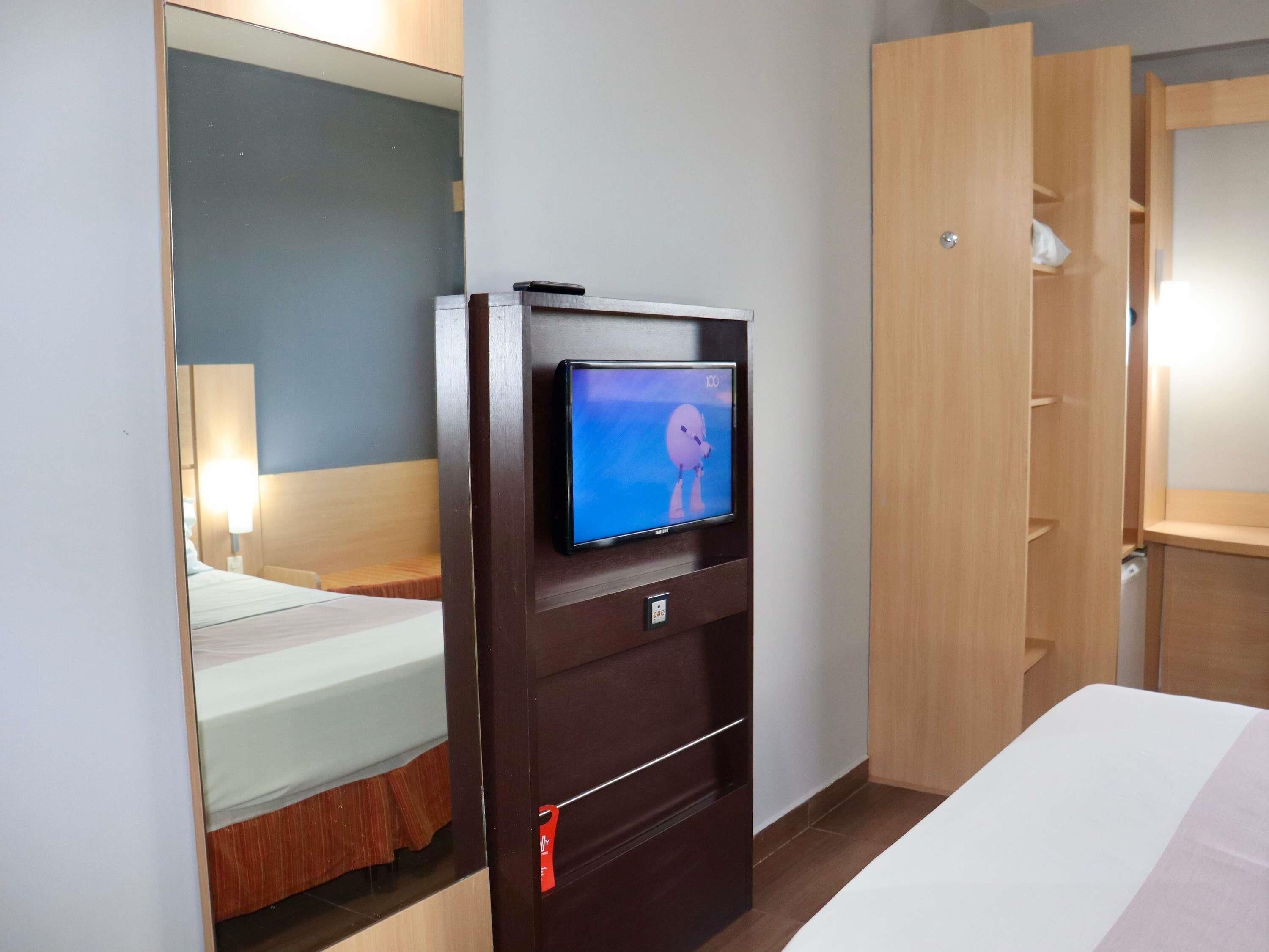 A hotel room with a bed, a TV mounted on a wooden cabinet, and a wardrobe.