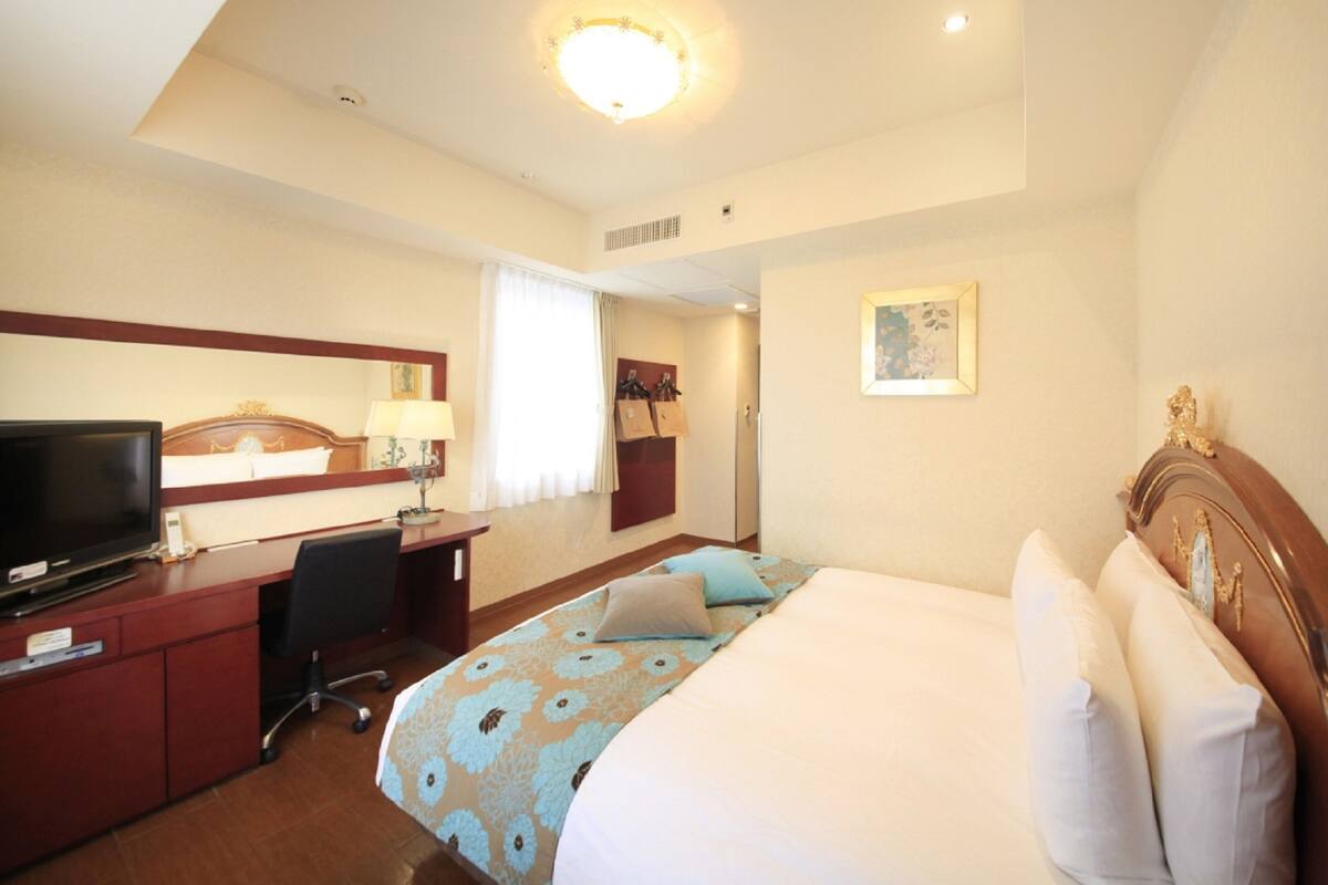 A hotel room with a bed, desk, television, and a painting on the wall.