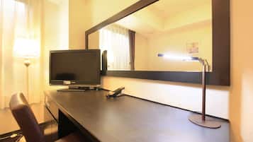 A hotel room with a desk, a television, a lamp, and a mirror.