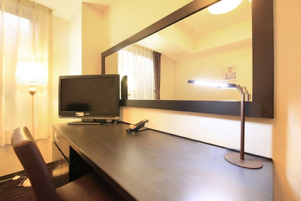 Una habitación de hotel con escritorio, televisión, lámpara y espejo.