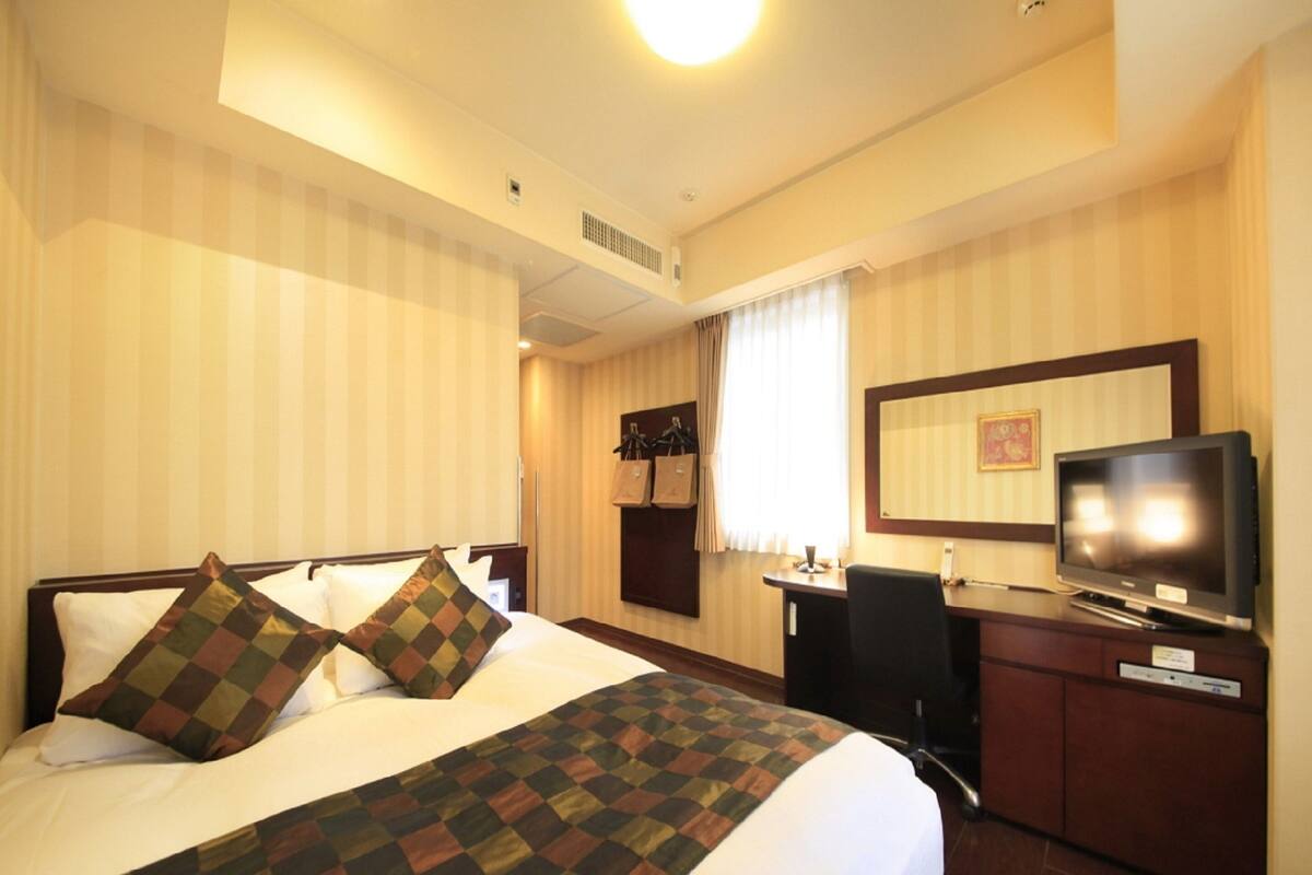 A hotel room with a large bed, a desk with a chair, a television, and a mirror on the wall.