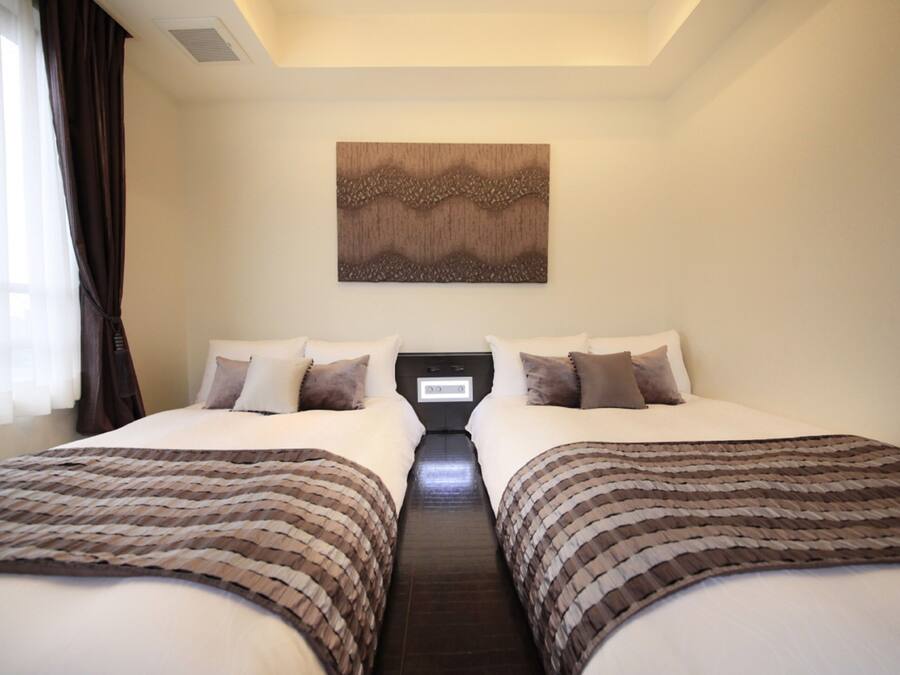 Quarto de hotel com duas camas, um relógio digital na parede e uma grande obra de arte abstrata sobre as camas.