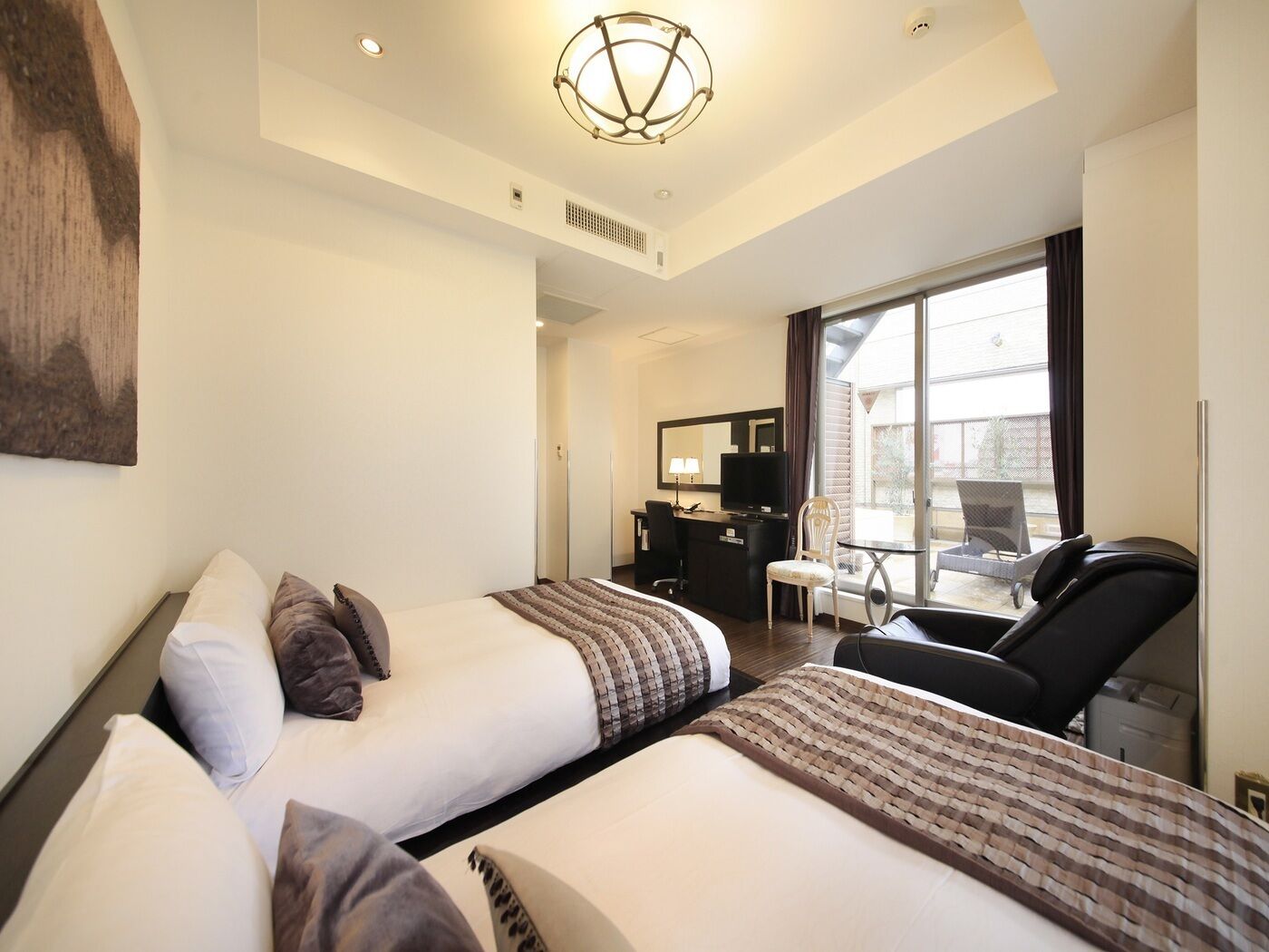A hotel room with two beds, a desk, a chair, and a large window.
