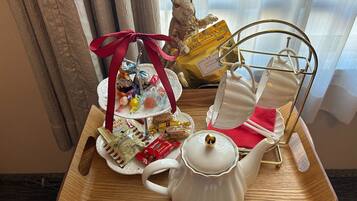 A tray with a white teapot, a tiered tray of assorted snacks, a decorative rabbit figurine, and a gold-colored bag of snacks.