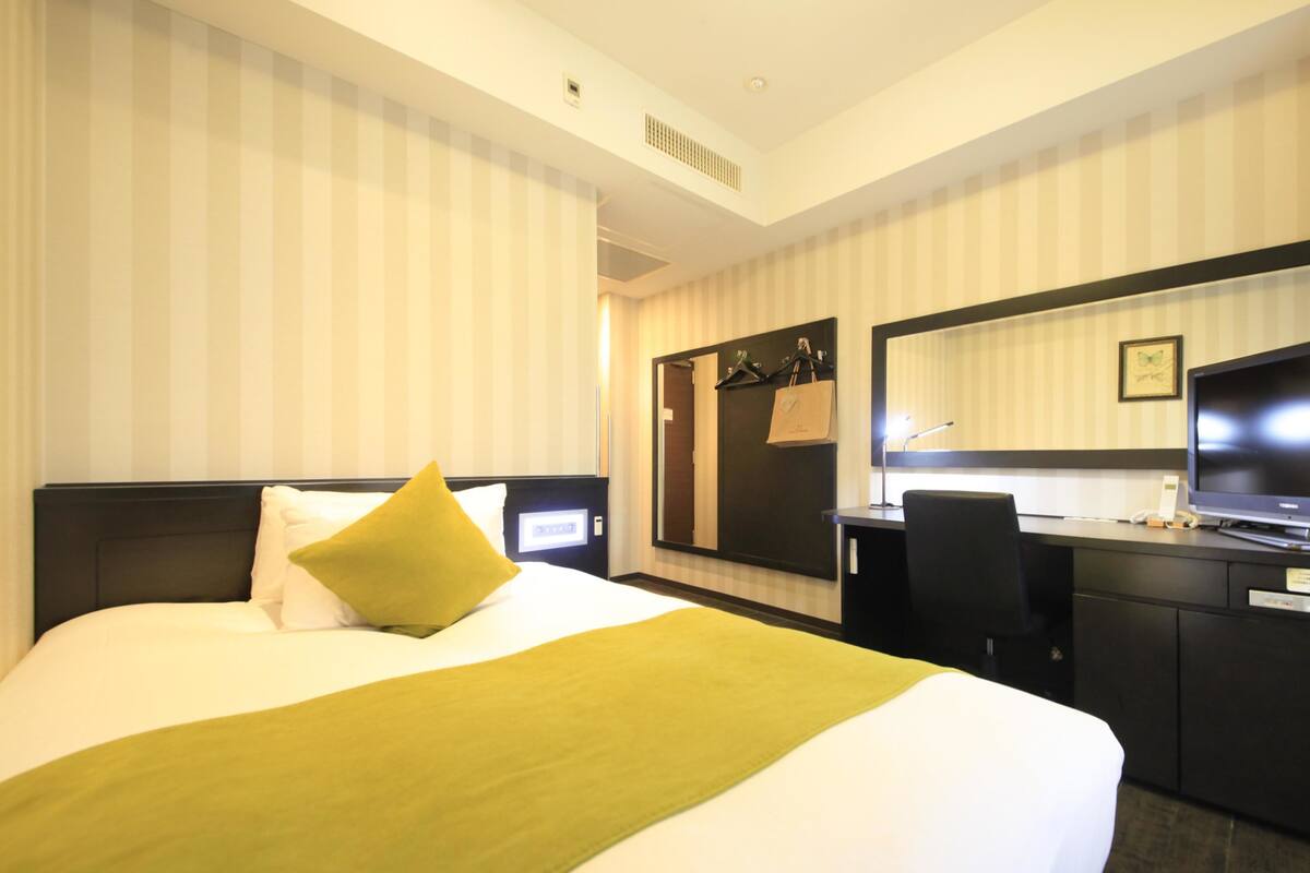 A hotel room with a bed, a desk, a chair, a mirror, and a wardrobe.