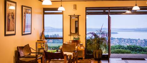 A room with a view of a body of water, a wooden bench, a chair, a small table, and a potted plant.