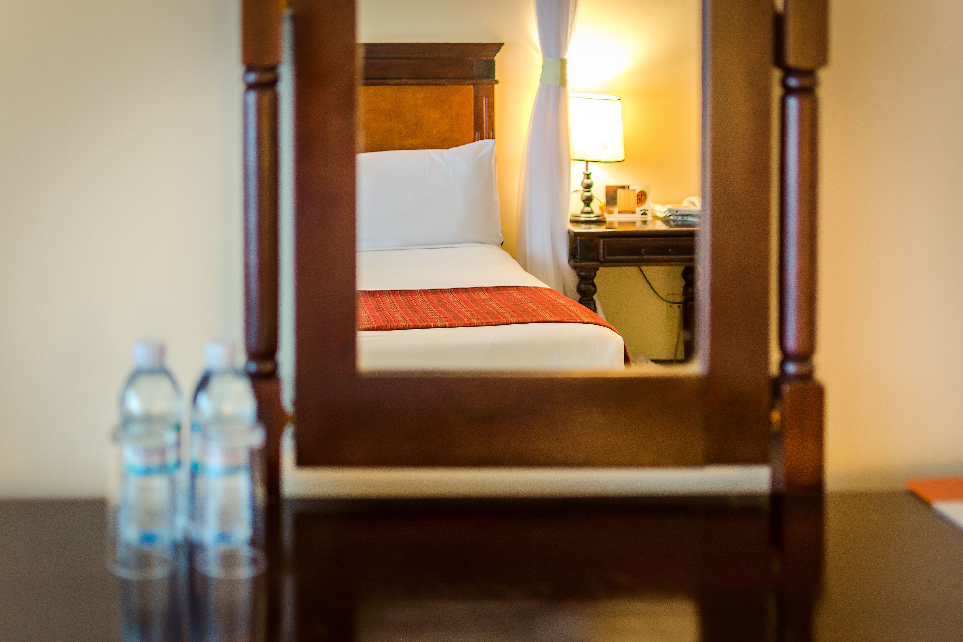Una habitación de hotel con cama, mesita de noche, lámpara y botellas de agua sobre la mesa.