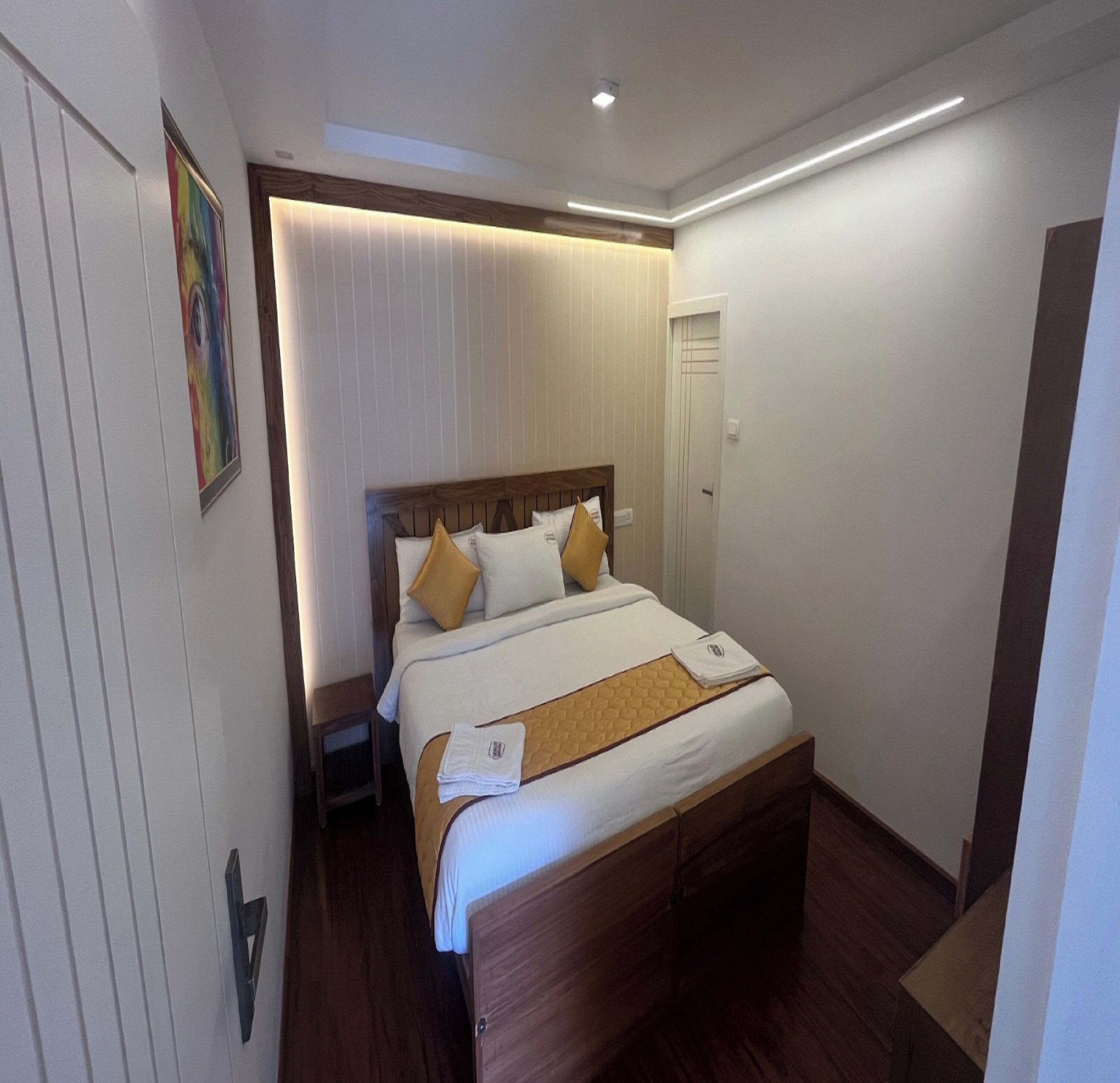 Un lit bien fait, avec une tête de lit en bois, une literie blanche et deux coussins décoratifs.