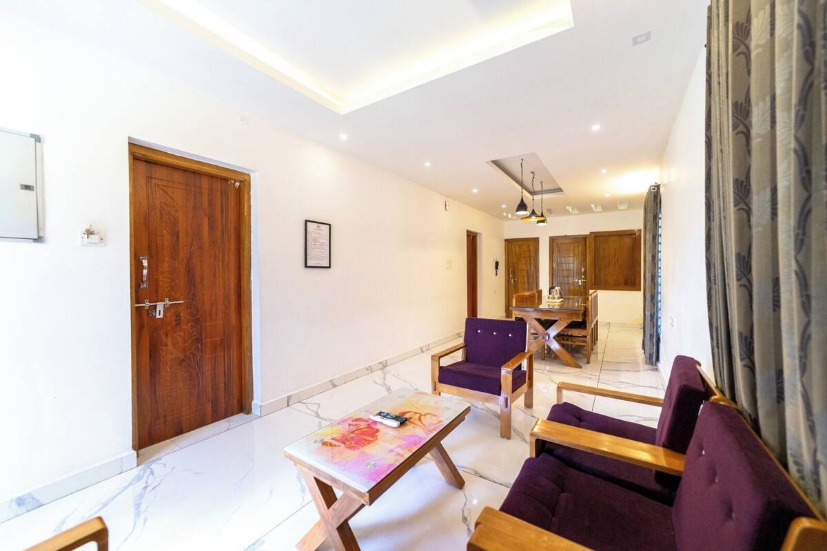 A spacious living area with a wooden door, a dining table with chairs, and a sofa.