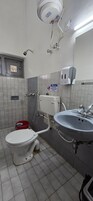 Een badkamer met toilet, wastafel en handdroger. Er hangt een bord aan de muur en er staat een rode emmer op de vloer.