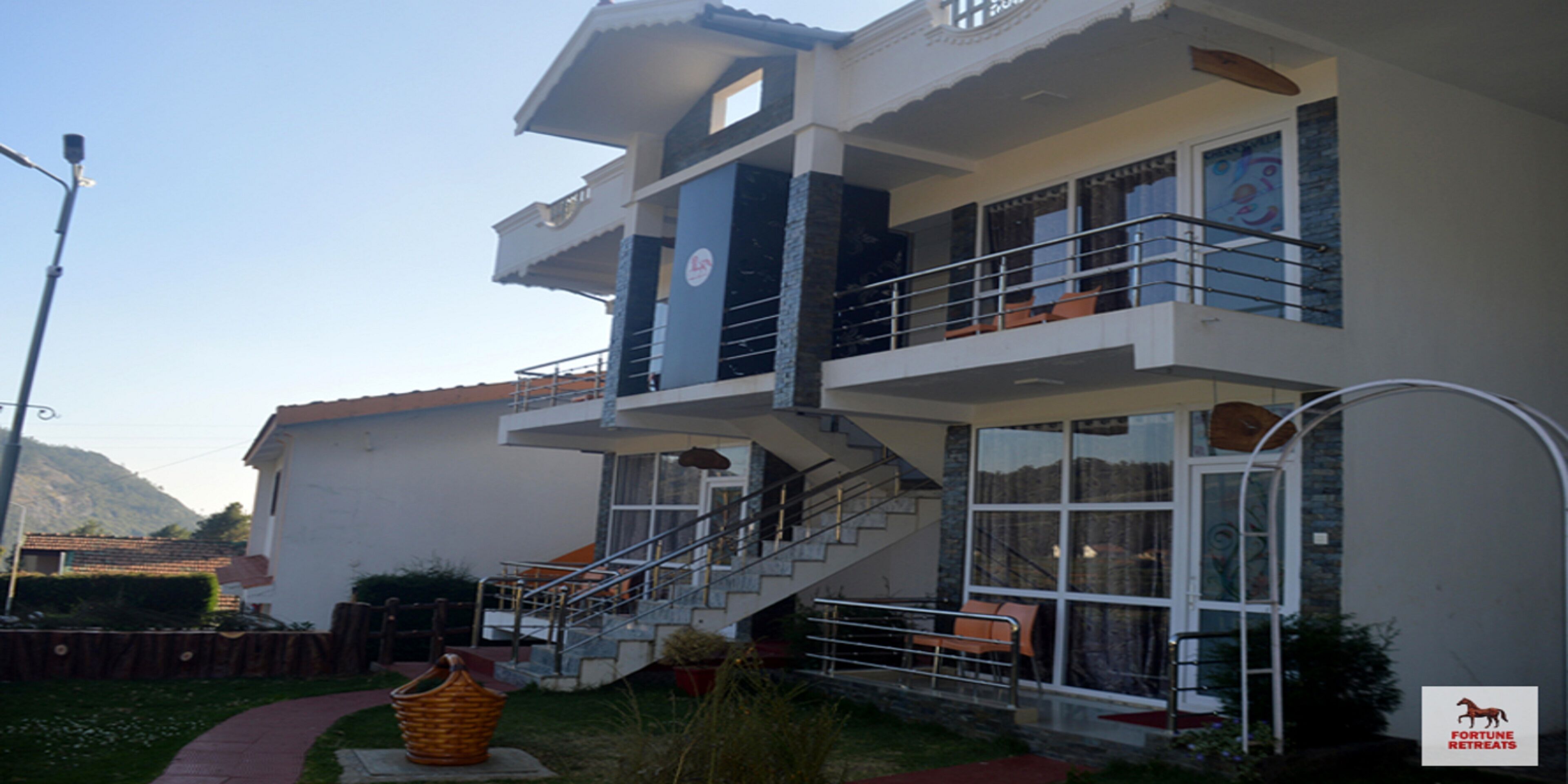 A multi-story building with a staircase leading to the upper floor. There is a balcony with a railing and a window with curtains.