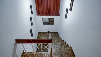 A staircase with wooden flooring and white walls, leading to a landing with a red curtain and framed pictures.