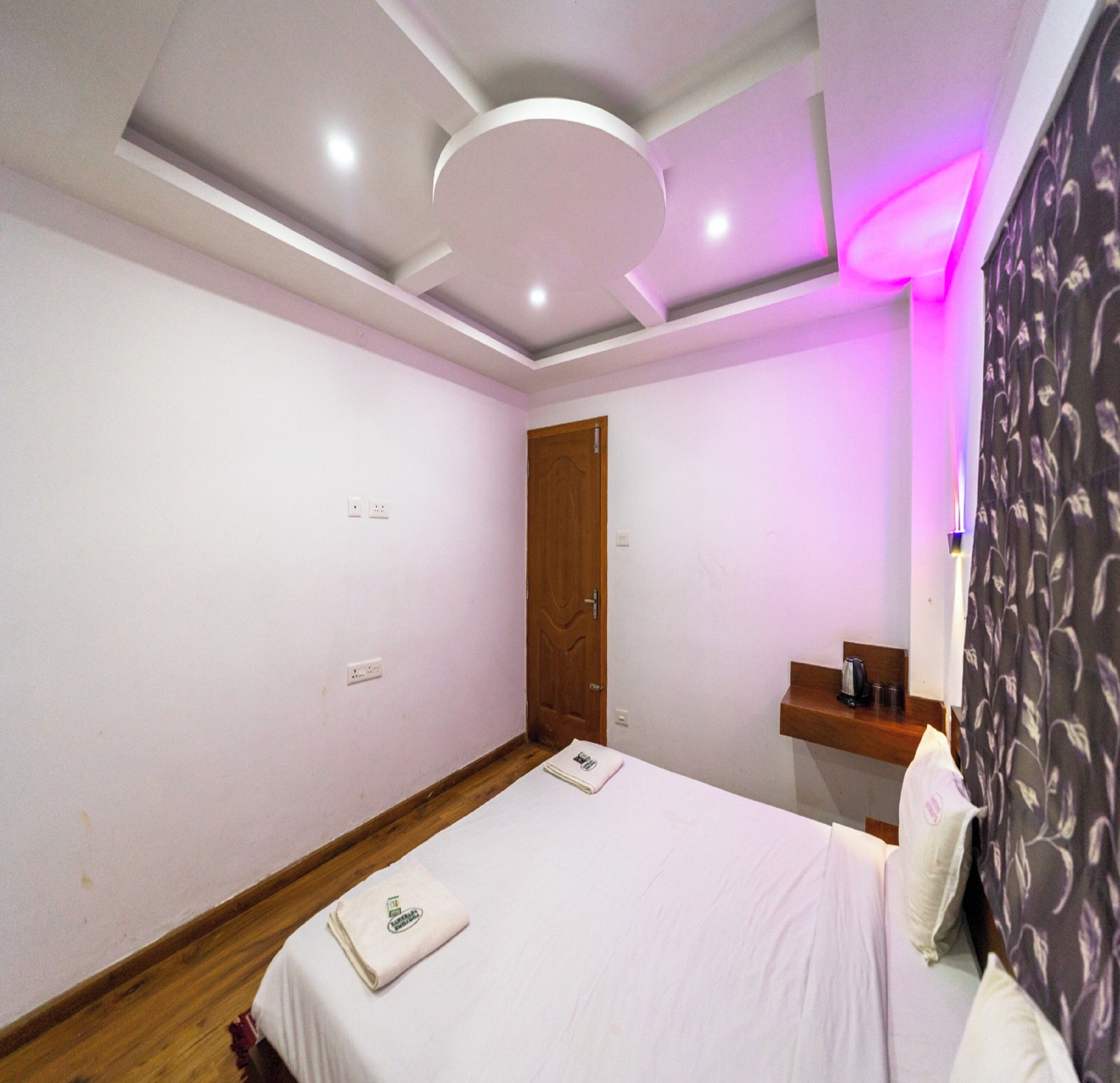 Un dormitorio con cama, una puerta de madera, un estante pequeño y una pared con toma de corriente.