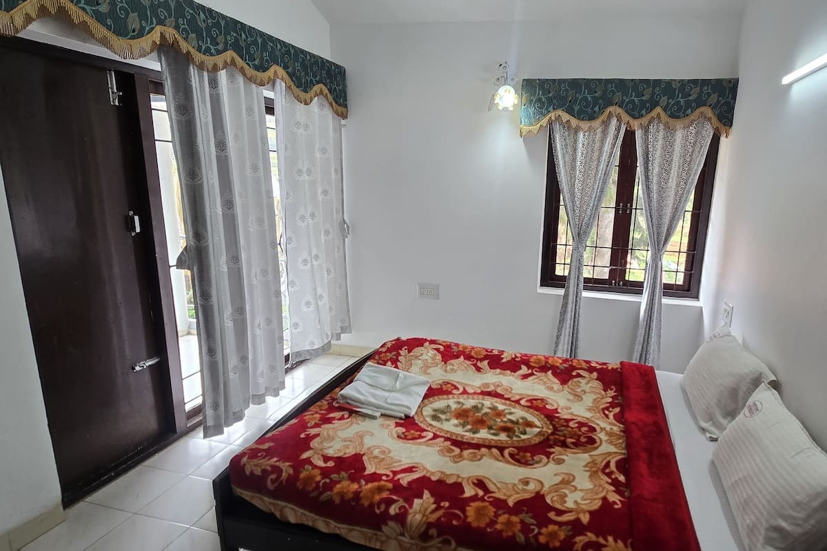 A bedroom with a bed, a window with curtains, a door, and a light fixture.
