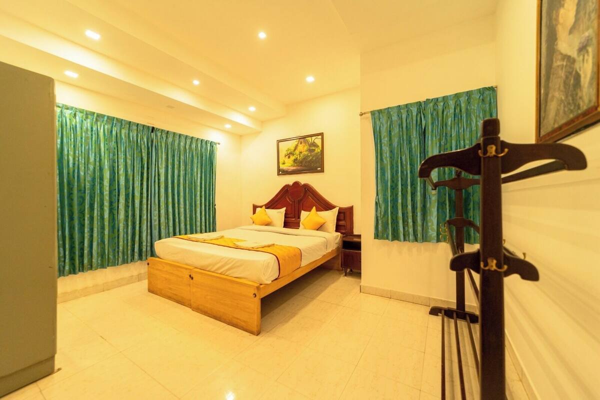 A bedroom with a wooden bed, green curtains, a painting on the wall, and a guitar stand.