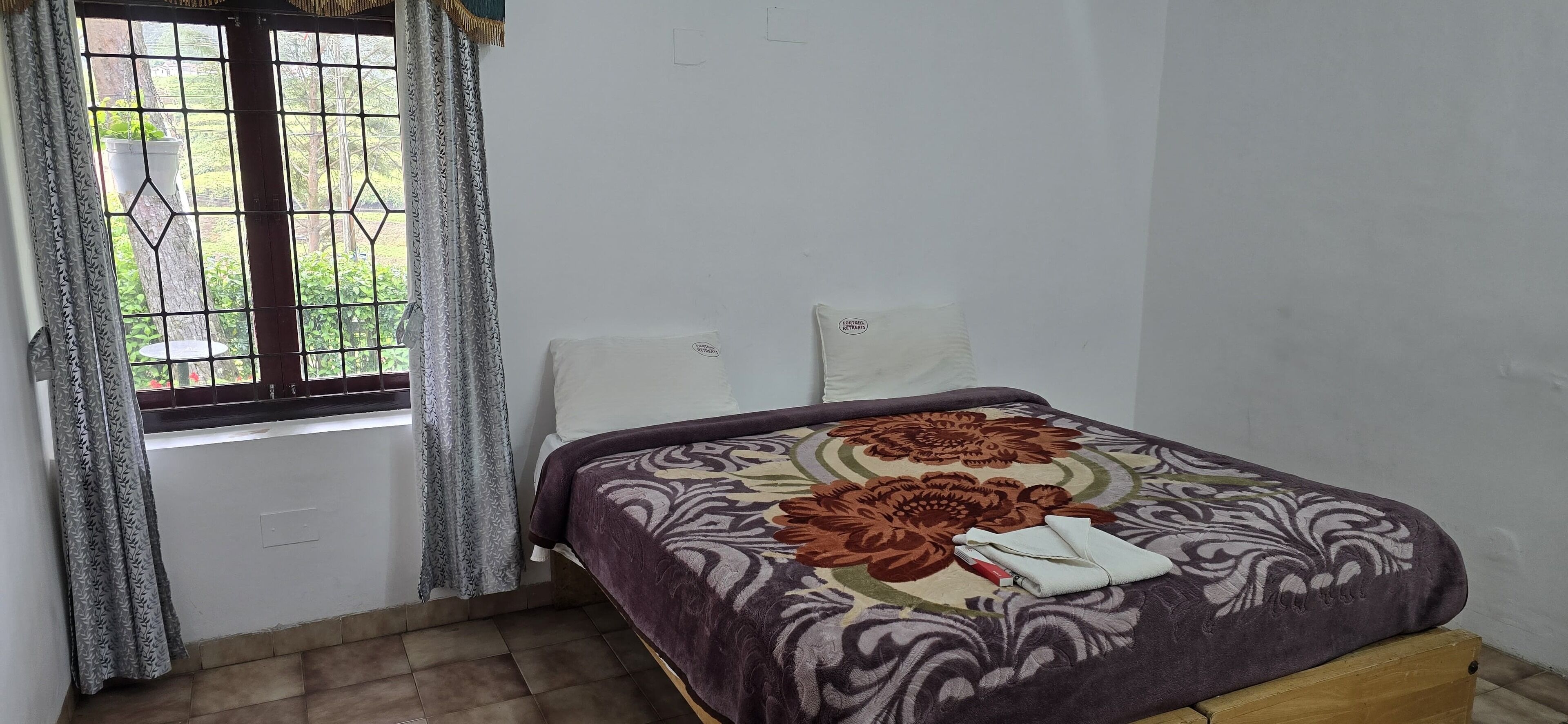 A bedroom with a bed, a window with curtains, and a view of greenery outside.